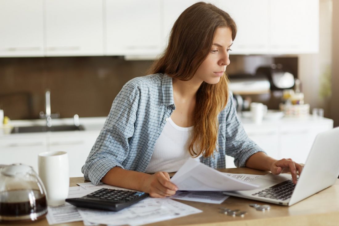 Person Using a Laptop Whilst Holding a Set of Papers In Their Other Hand