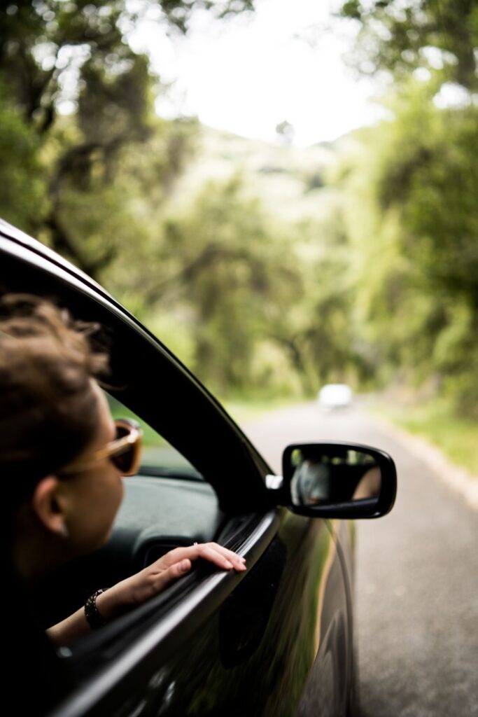 Someone wearing sunglasses looking out of the passengers black car window whilst driving on a country road